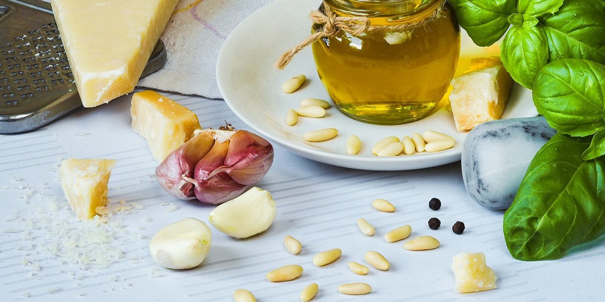 Olio extravergine, basilico, formaggio e pinoli disposti sul tavolo